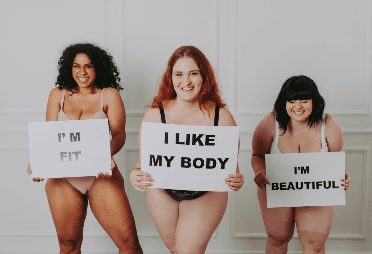 Drei Frauen mit Schildern ‚I’m Fit‘, ‚I Like My Body‘, ‚I’m Beautiful‘ – Symbol für Selbstvertrauen und Selbstbewusstsein.