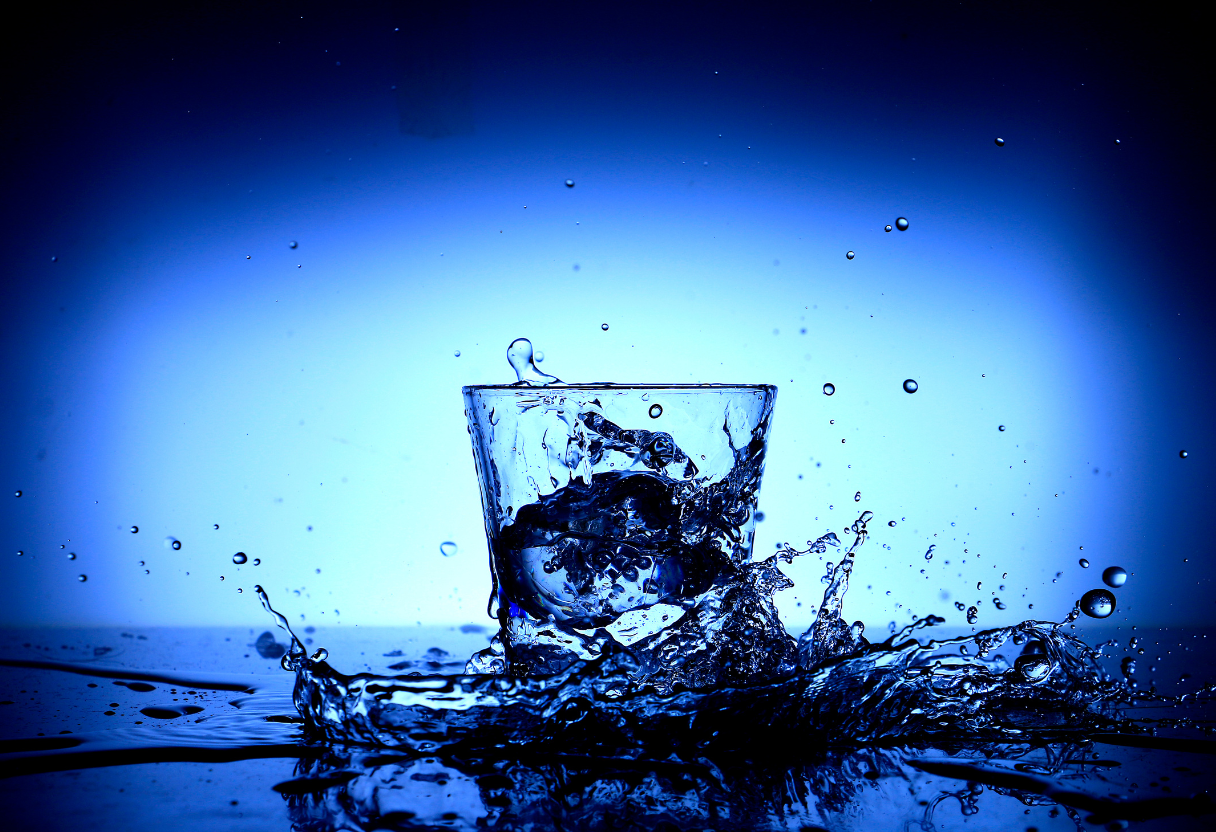 Ein Glas mit spritzendem Wasser vor einem blauen Hintergrund