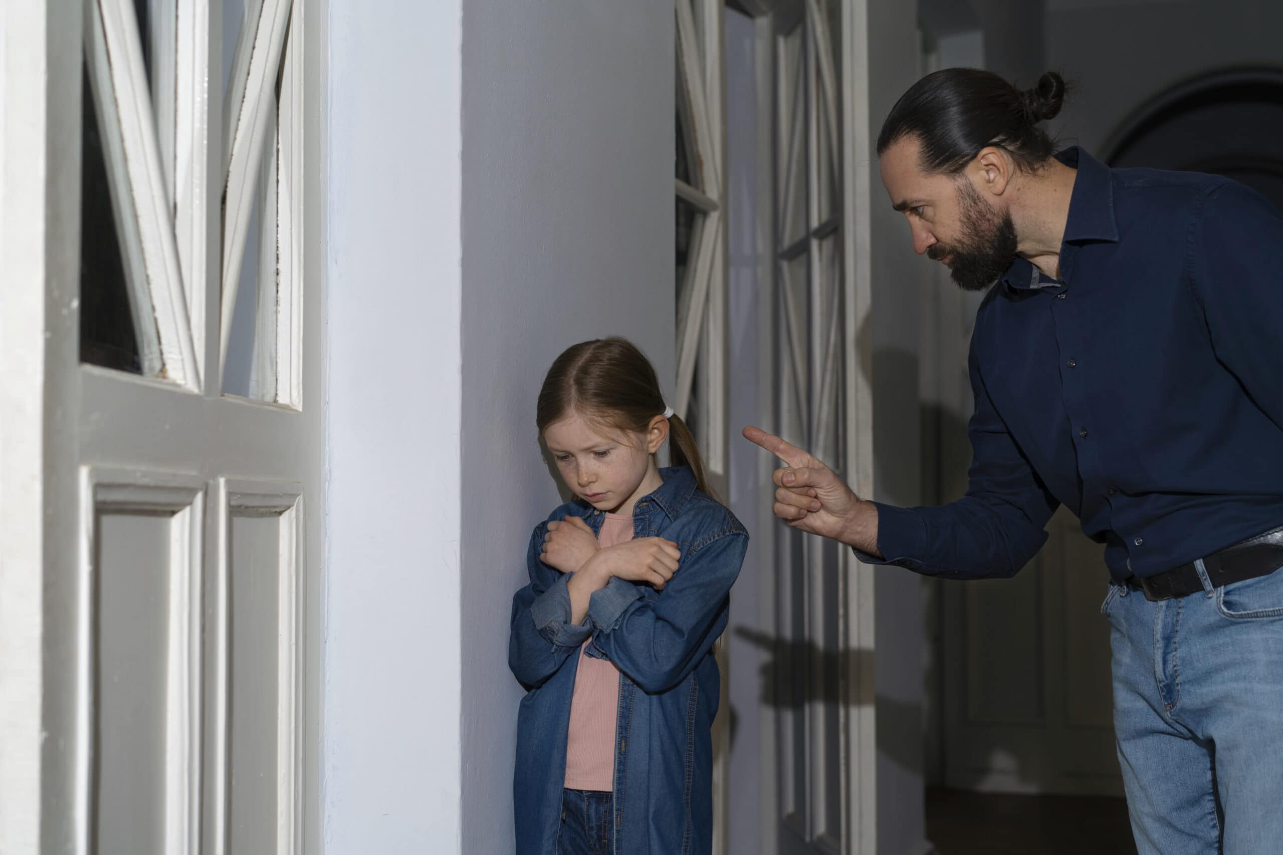 Erwachsener schimpft mit Kind, das verängstigt an der Wand steht