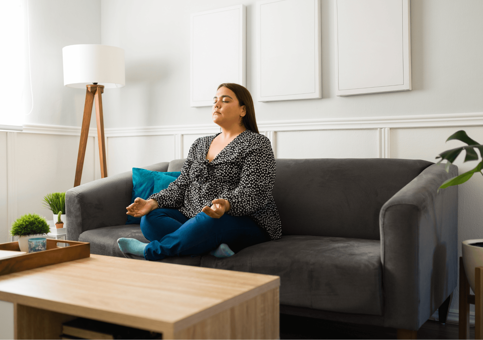 Frau meditiert im Schneidersitz auf einem Sofa zu Hause – Symbol für Achtsamkeit im Alltag