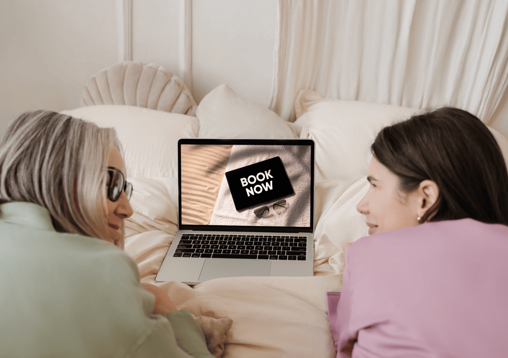 Zwei Frauen liegen im Bett und schauen auf einen Laptop mit der Aufschrift „Book Now“