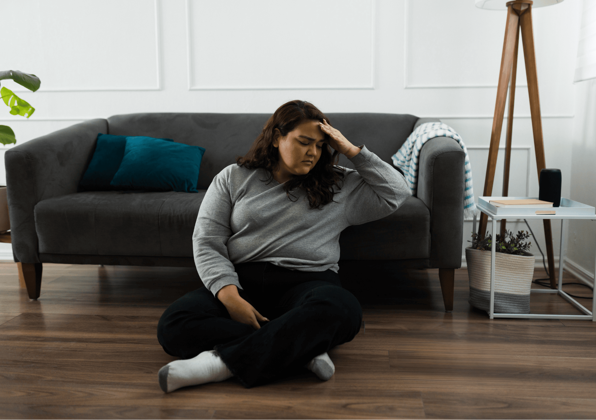 Erschöpfte Frau mit Selbstzweifeln sitzt auf dem Boden vor dem Sofa