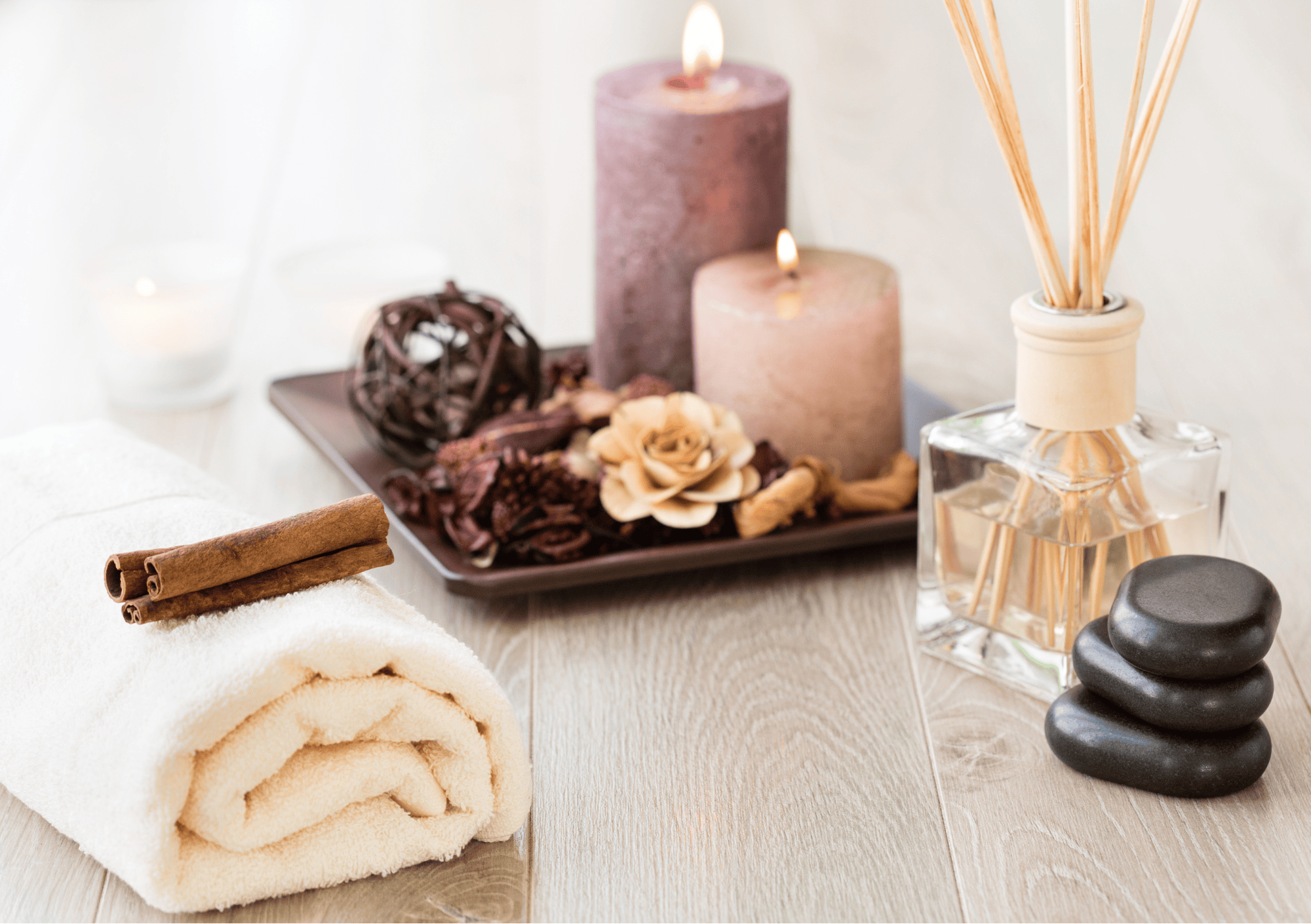 Wellness-Arrangement mit Handtuch, Duftkerzen, Aroma-Diffuser und Dekoration auf hellem Holzboden