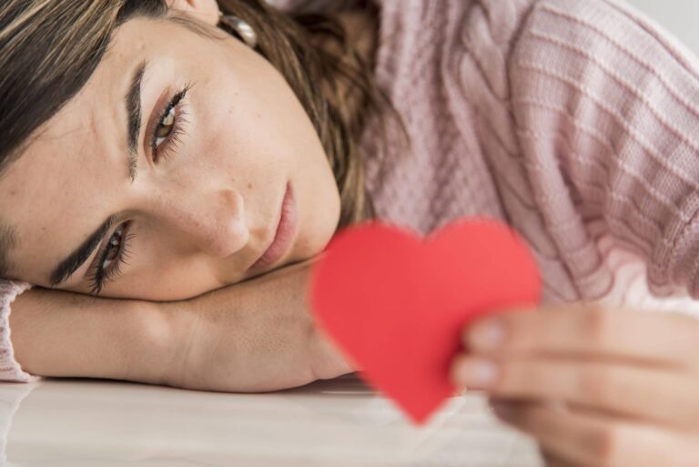 Junge Frau blickt nachdenklich auf ein rotes Herz und reflektiert über Selbstliebe