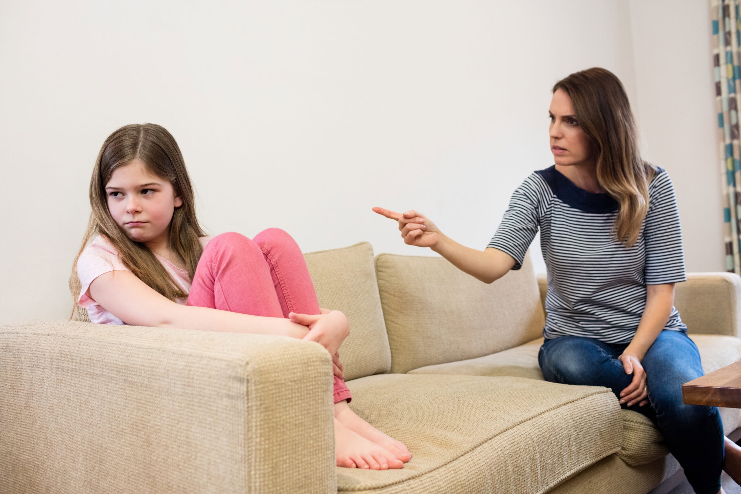 Mutter schimpft mit ihrer Tochter, die traurig auf dem Sofa sitzt