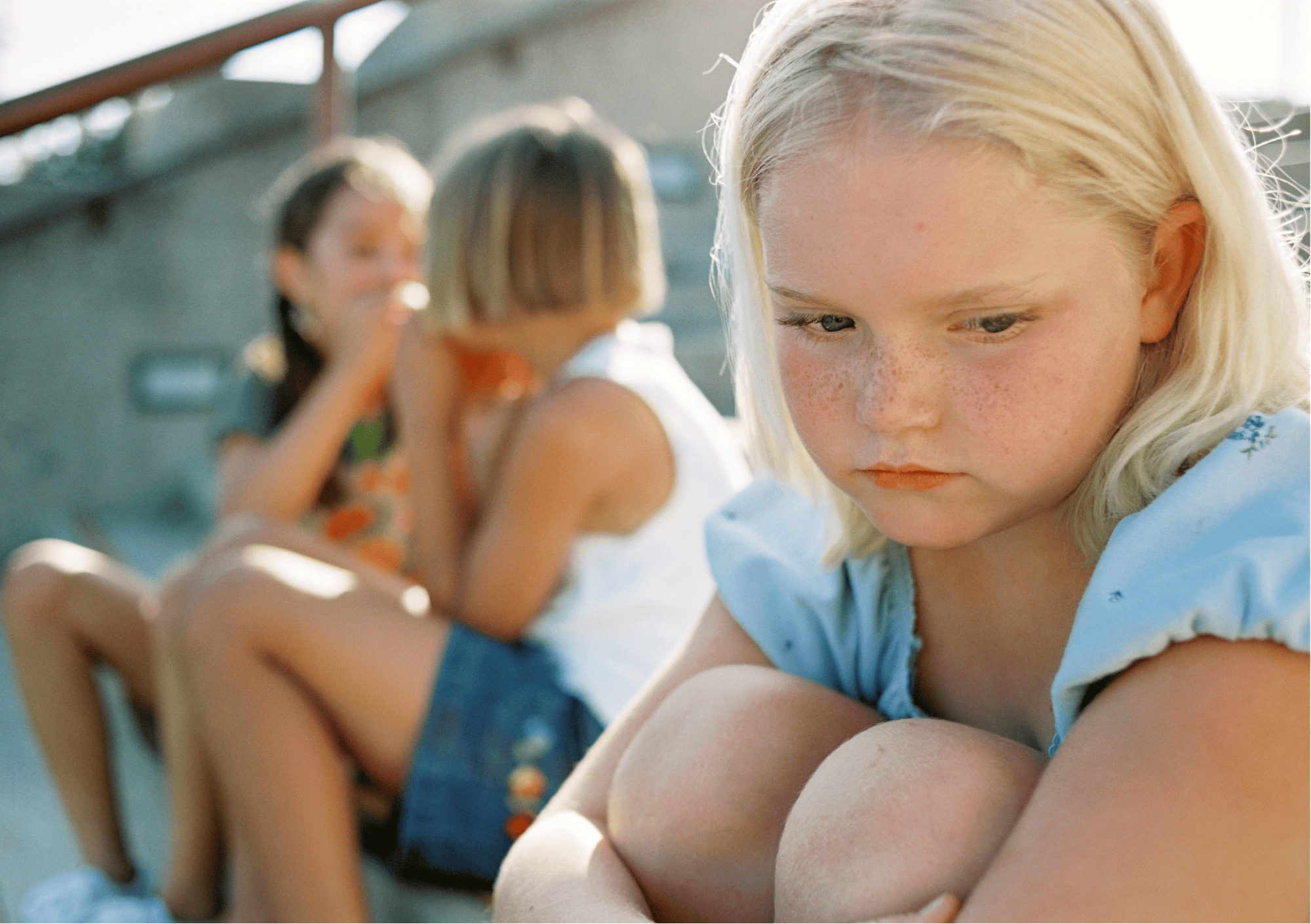 Trauriges Mädchen sitzt allein, während andere Kinder tuscheln – Symbol für Ausgrenzung