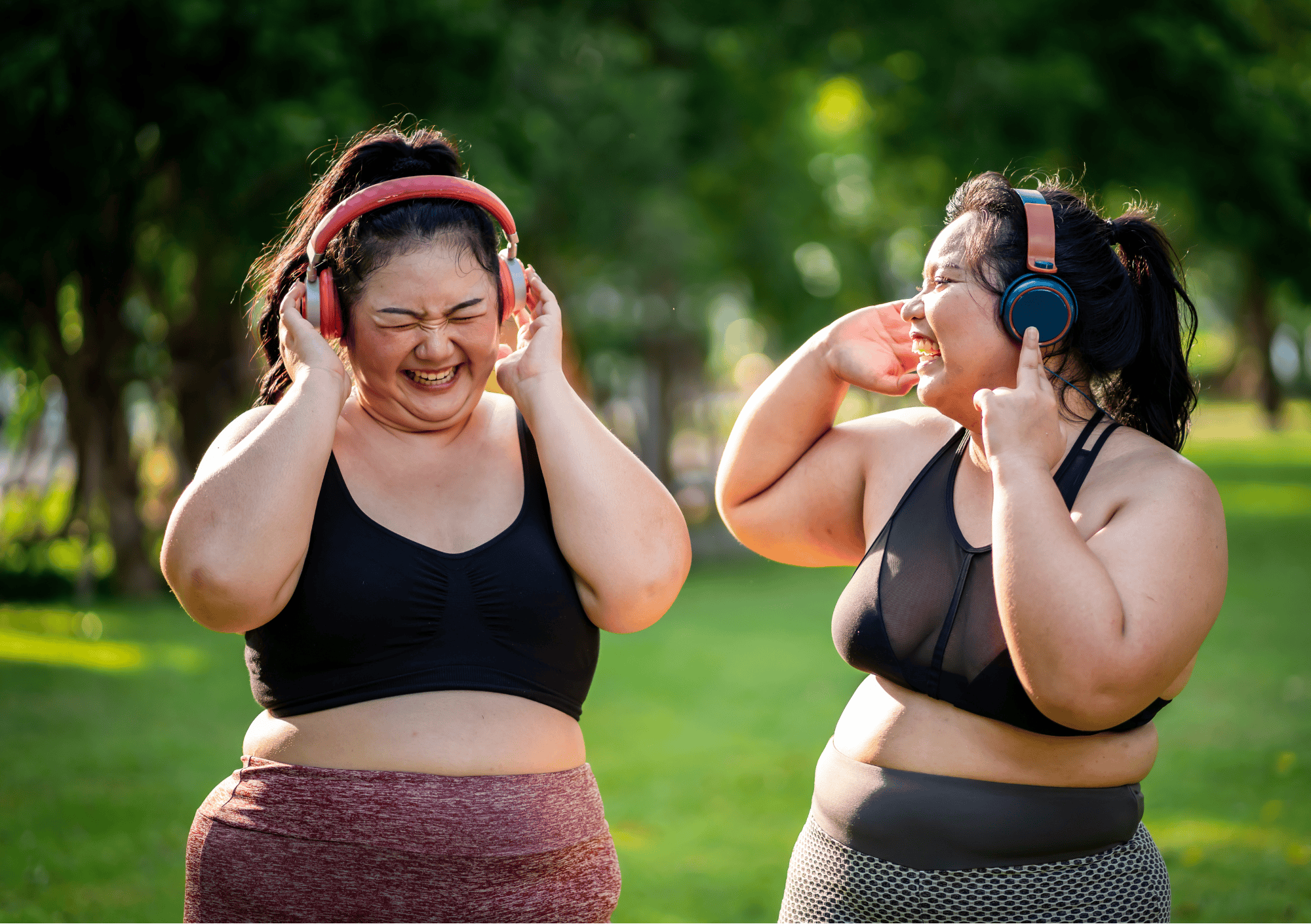 Zwei fröhliche Frauen mit Kopfhörern in Sportkleidung genießen Musik beim Outdoor-Workout