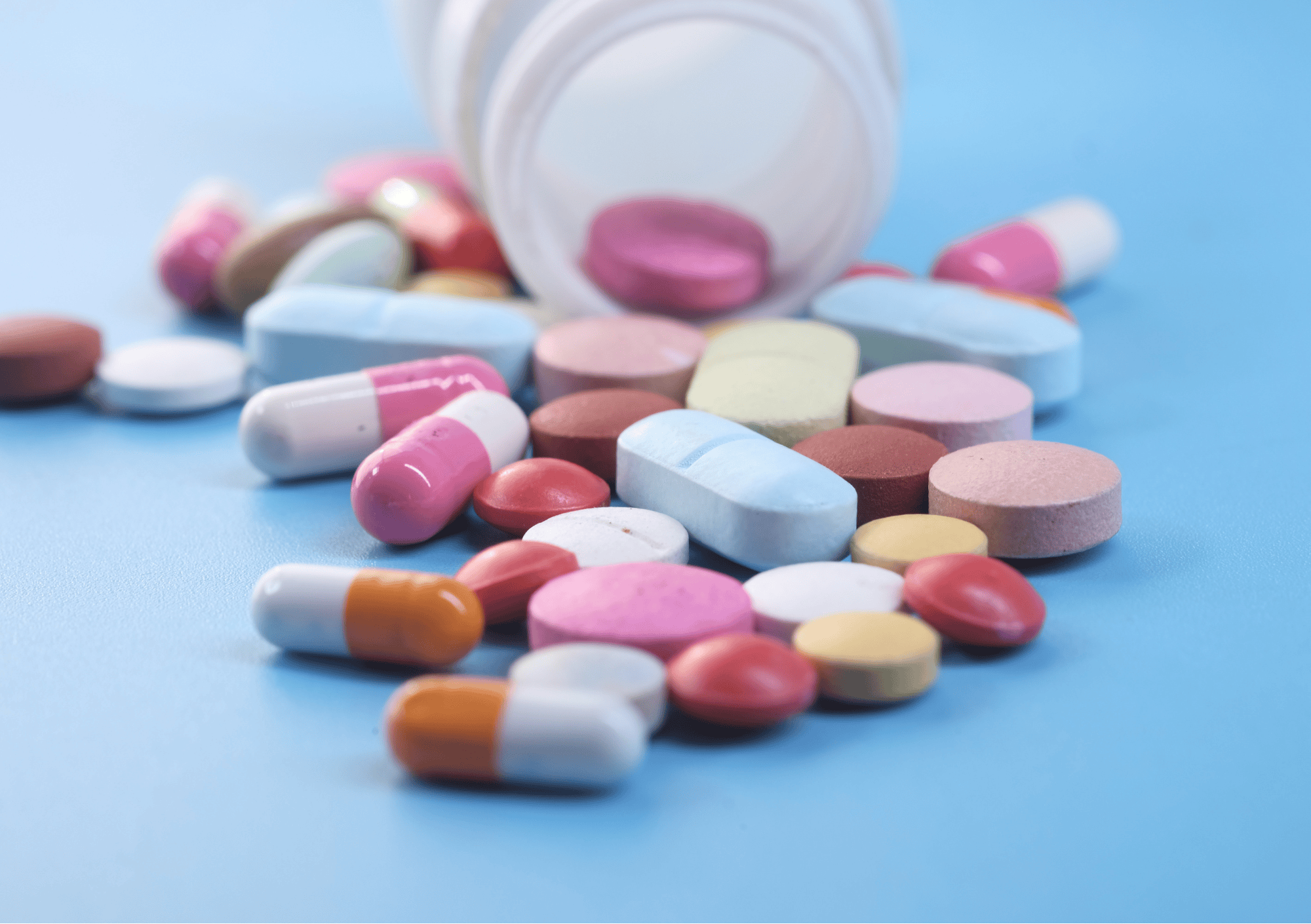 Verschiedene bunte Tabletten und Kapseln liegen verstreut vor einem offenen Behälter