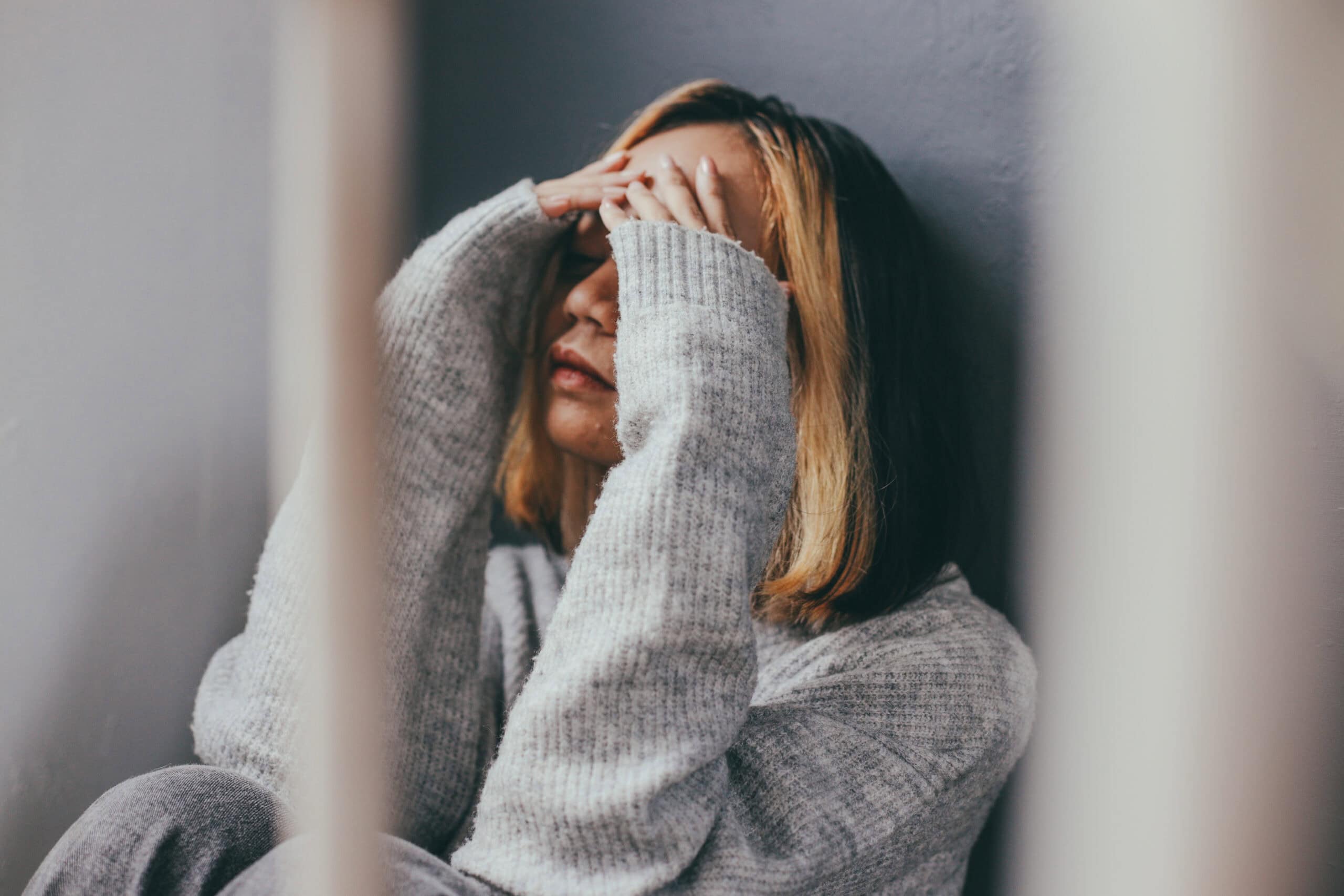 Frau hält den Kopf in den Händen und sitzt verzweifelt am Boden – Symbol für Selbsthass und Depression