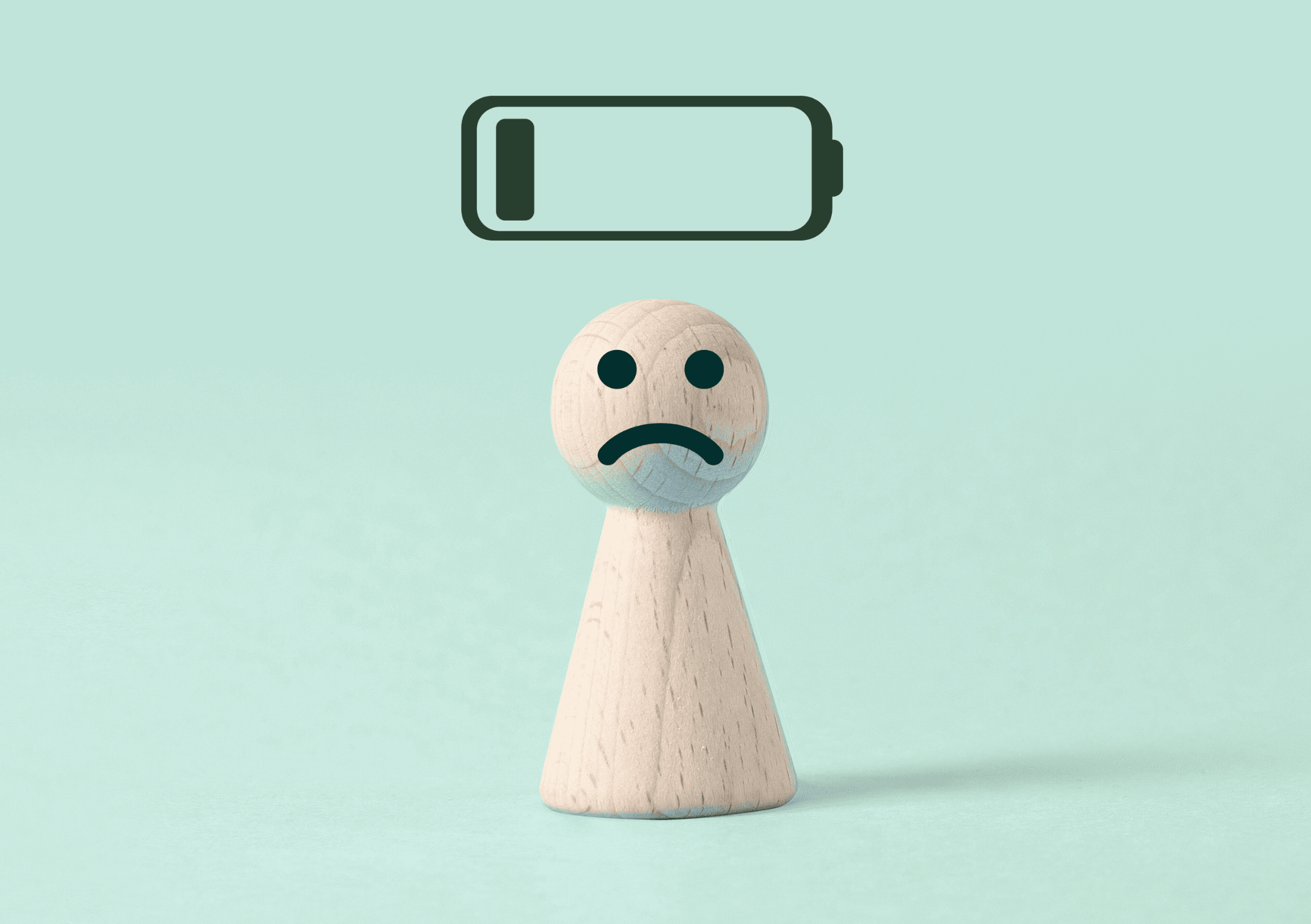 Holzfigur mit traurigem Gesicht und leerem Batteriesymbol als Zeichen für Stress und Erschöpfung