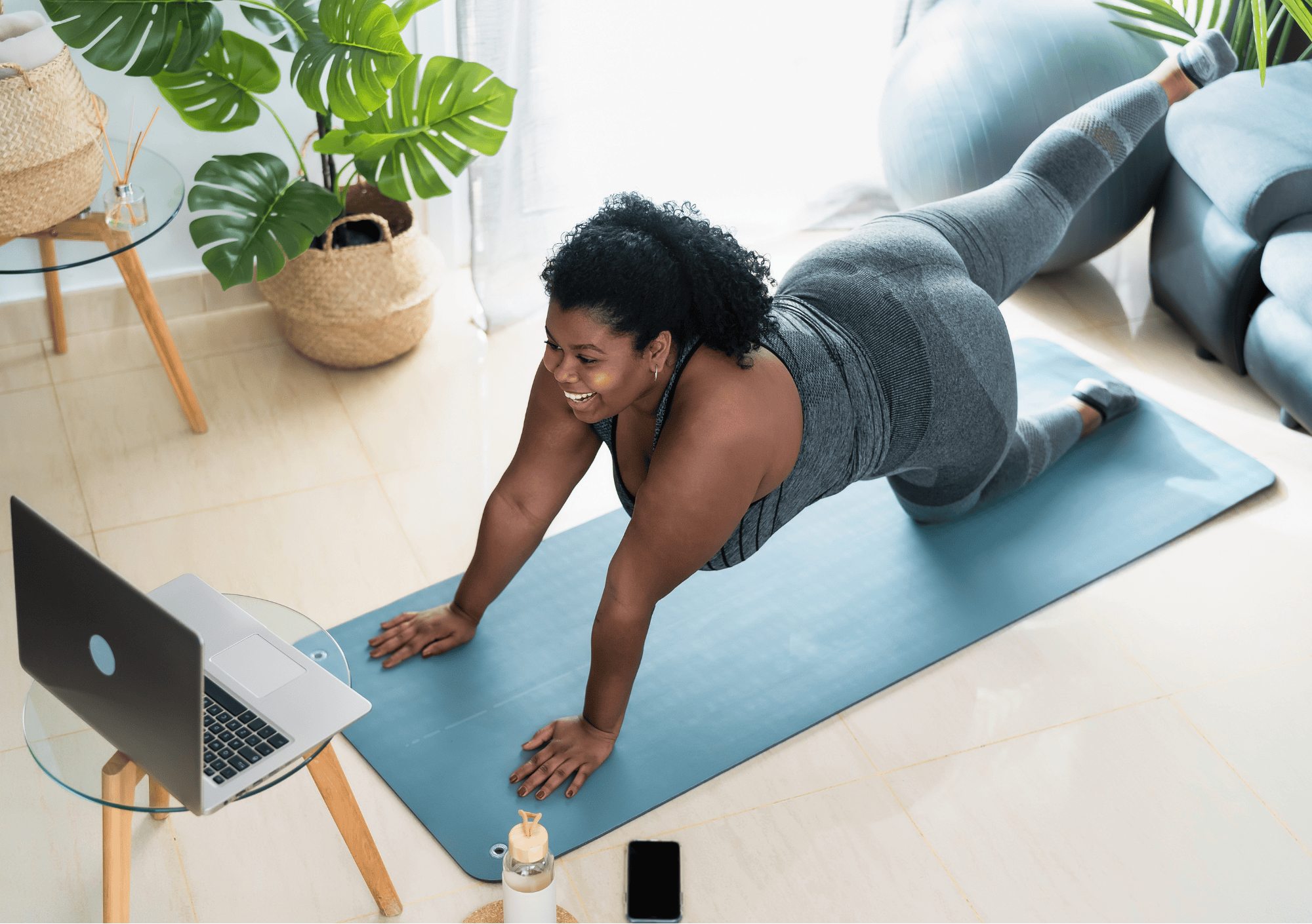 Frau trainiert lächelnd auf der Matte vor dem Laptop – Bewegung in Einklang mit Körperakzeptanz