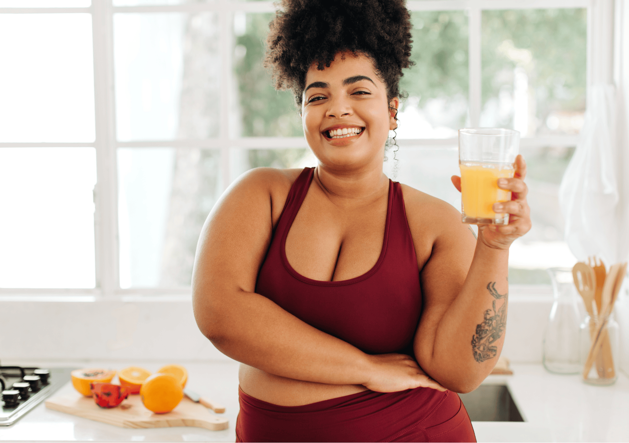 Lachende Frau in Sportkleidung mit Orangensaft in der Küche – Symbol für Selbstfürsorge