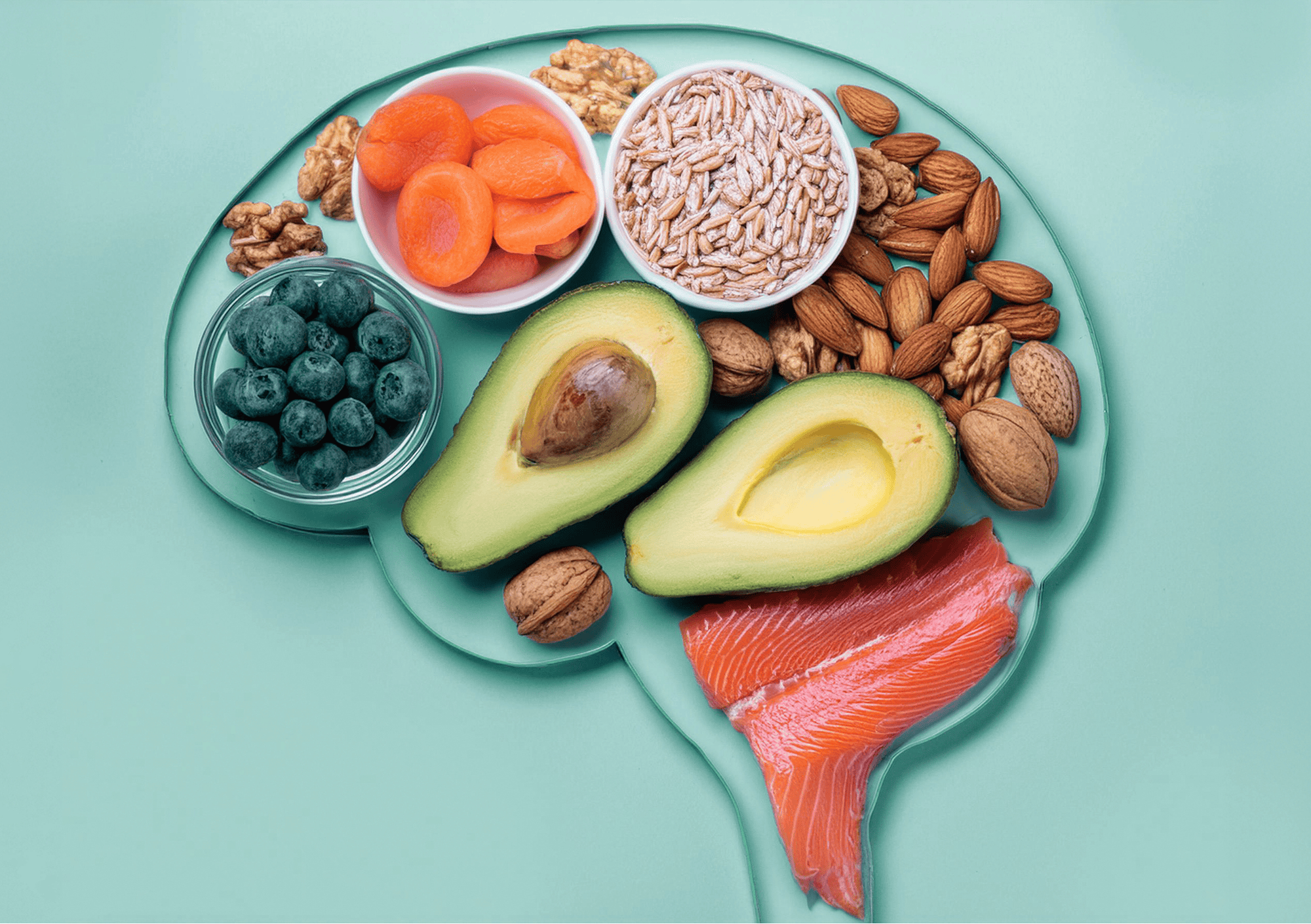 Gesunde Langzeit-Sattmacher wie Avocado, Lachs, Nüsse und Hafer in Gehirnform angeordnet