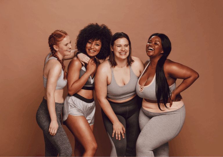 Vier Frauen unterschiedlicher Figur lachen zusammen und zeigen gelebte Körperakzeptanz
