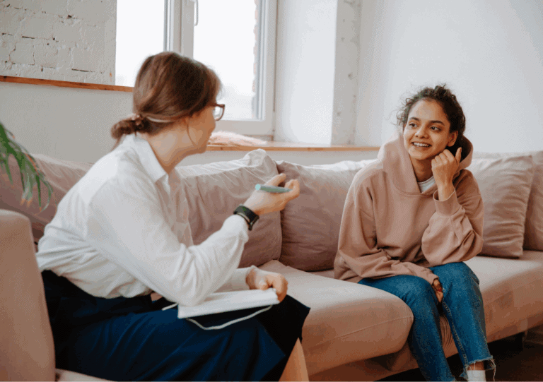 Coach spricht mit junger Frau über Selbstliebe in entspannter Atmosphäre auf dem Sofa