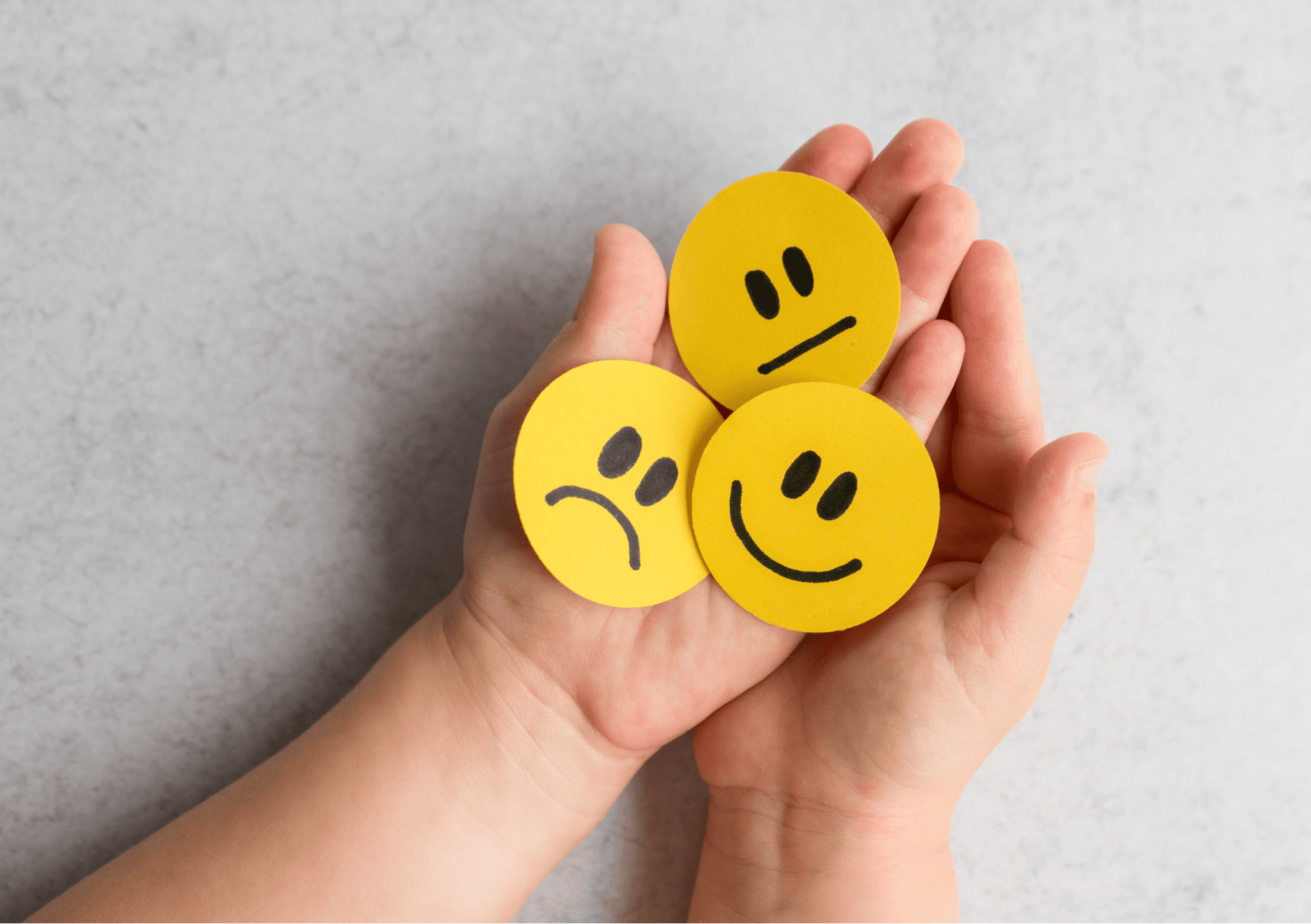 Kinderhände halten drei gelbe Smileys mit verschiedenen Gesichtsausdrücken zur Gefühlsregulation