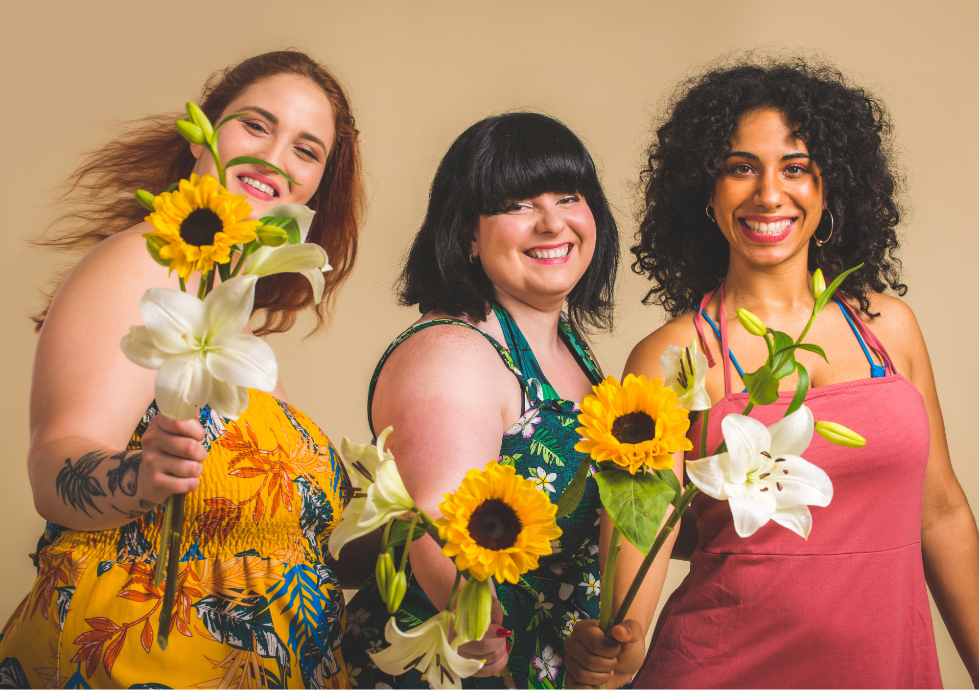 Drei lächelnde Frauen mit Blumen stehen für Körper annehmen, Selbstliebe und Körperakzeptanz