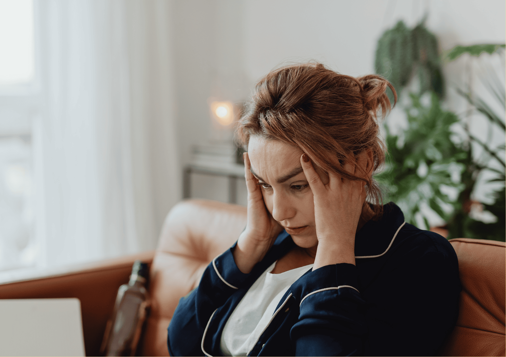 Frau sitzt mit gestresstem Gesichtsausdruck auf dem Sofa und hält sich den Kopf vor Überforderung