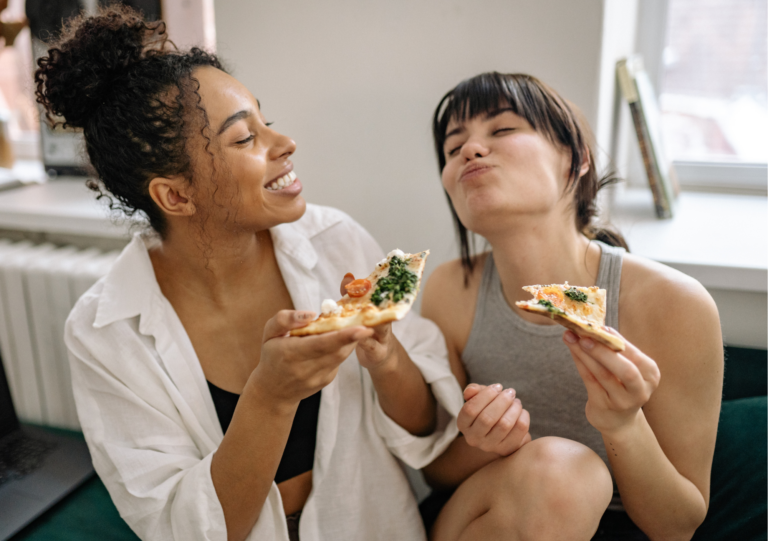 Zwei Frauen essen entspannt Pizza und lachen beim intuitiven Essen zu Hause