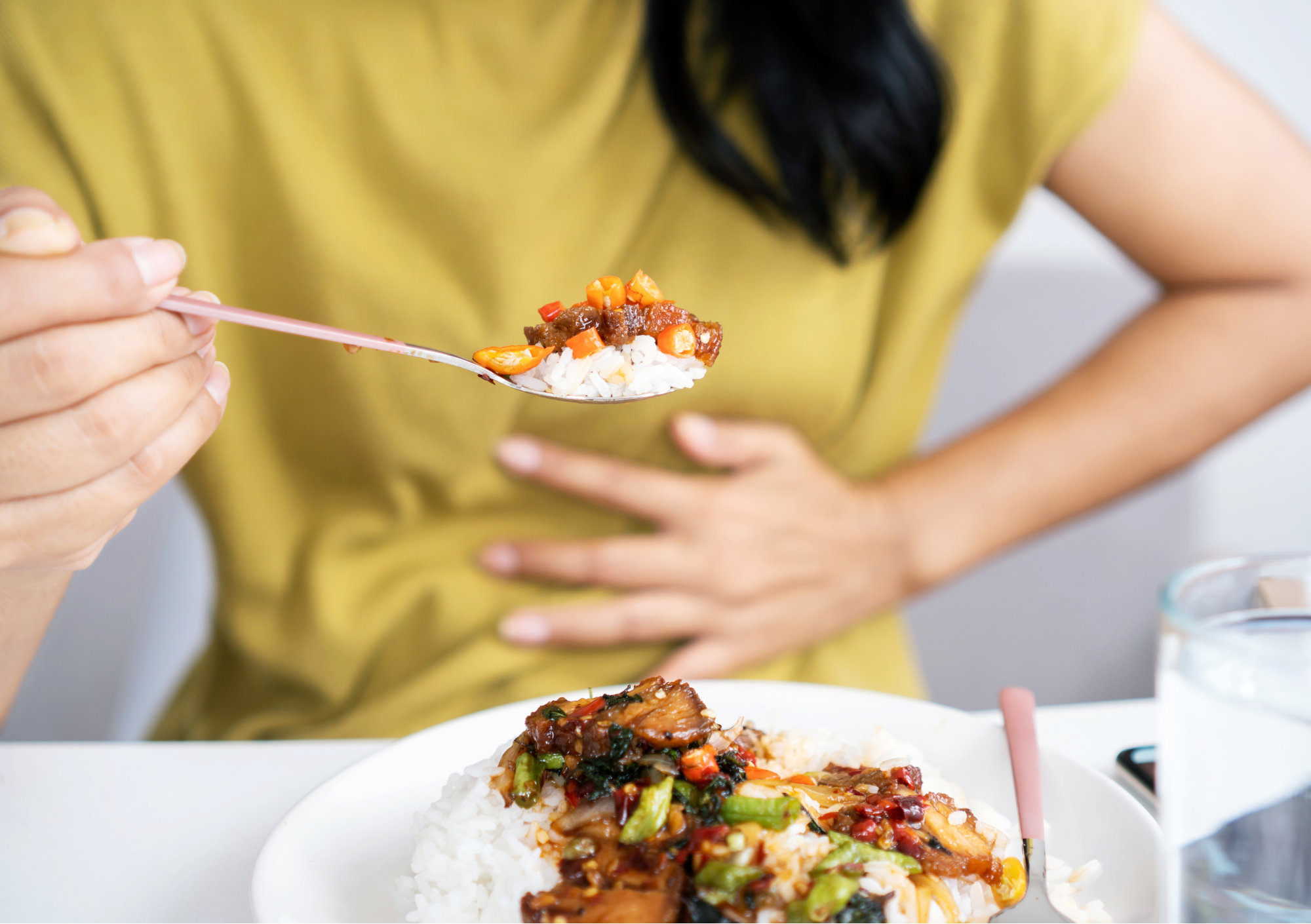 Person hält Löffel mit Essen und fasst sich an den Bauch als Zeichen von Esssucht und Unwohlsein
