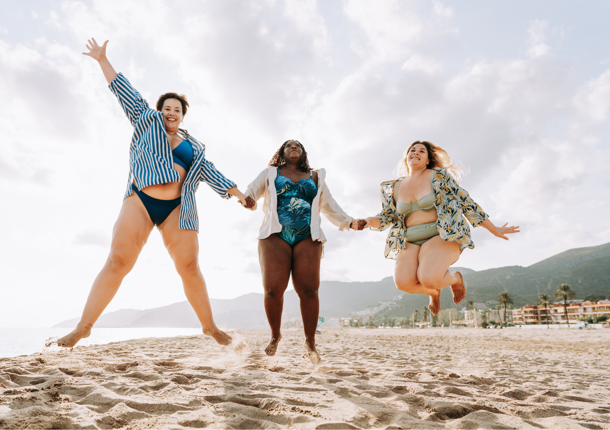 Drei Frauen springen lachend am Strand und feiern Body Positivity sowie Selbstakzeptanz